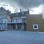 Brown house with a porch, many windows, and asphalt front.