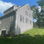 A gray house's siding with windows and a very neat and green lawn.